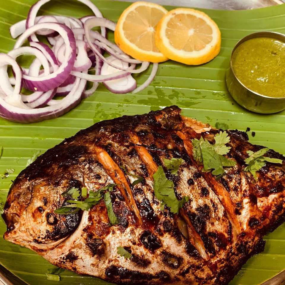Grilled fish garnished with cilantro, served on a banana leaf with sliced red onion, lemon, and green sauce.