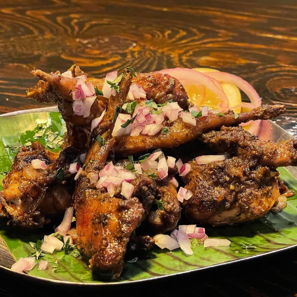 Spiced roasted chicken pieces garnished with chopped onions and herbs, served on a banana leaf-lined plate.